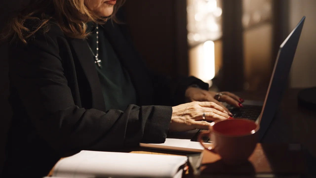 Personne travaillant sur un ordinateur portable à son bureau, à côté de carnets et d'une tasse