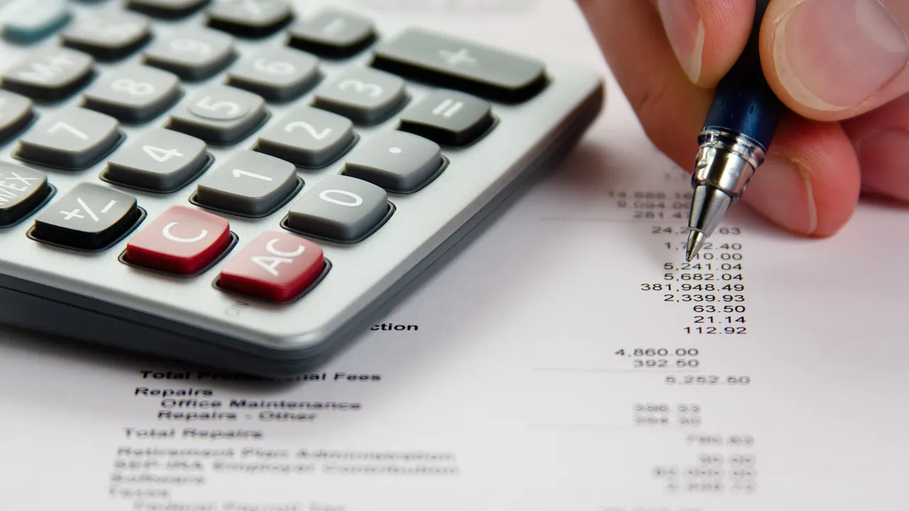 Calculatrice et main tenant un stylo sur un état financier imprimé