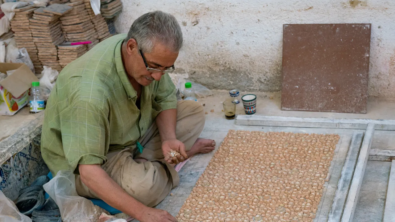 Artisan zelligeur assemblant une mosaïque de carreaux de céramique dans un atelier de Fès