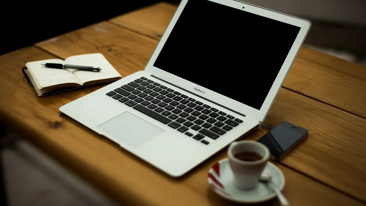 Ordinateur portable ouvert sur un bureau en bois, à côté d'un carnet, d'un smartphone et d'un café
